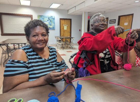 Two older adult participants crocheting together.