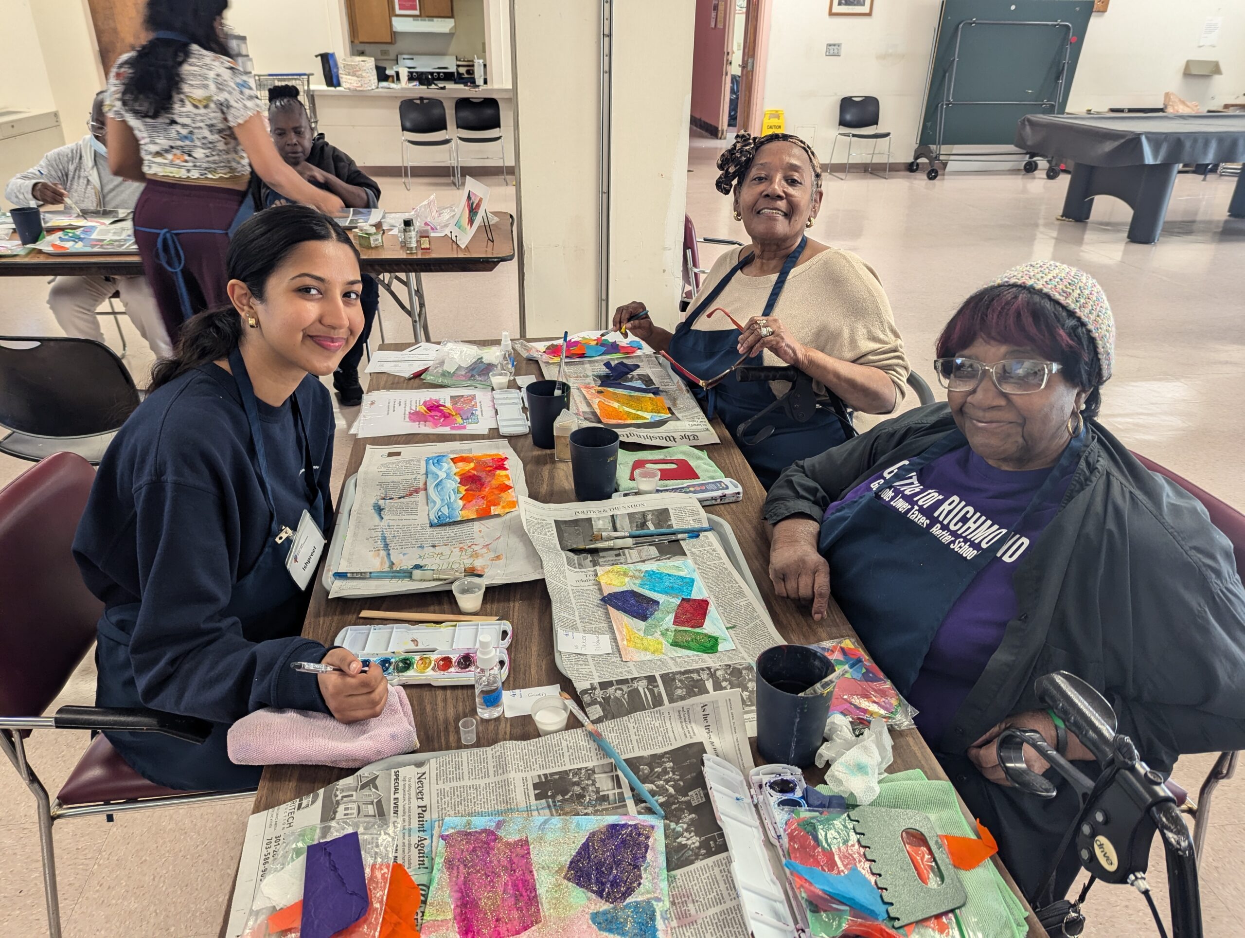 Two older participants and a volunteer do a newspaper painting activity.