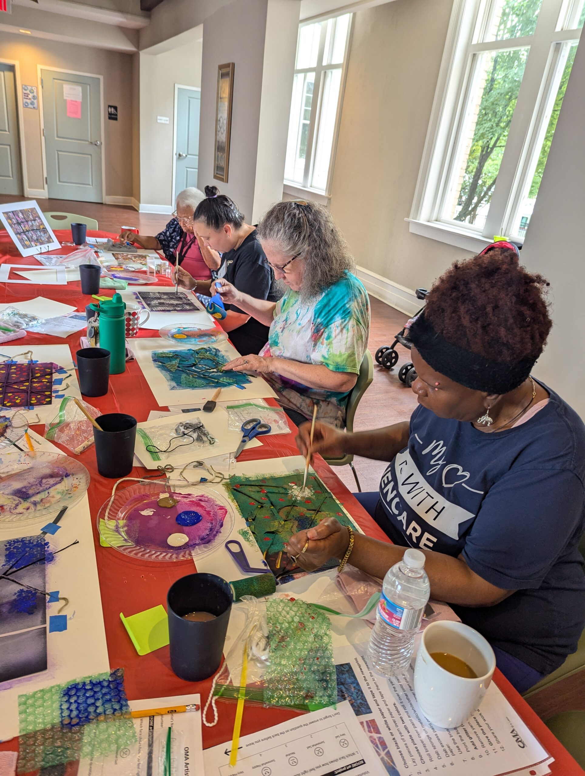 Older participants gather at a table to do a group painting activity.