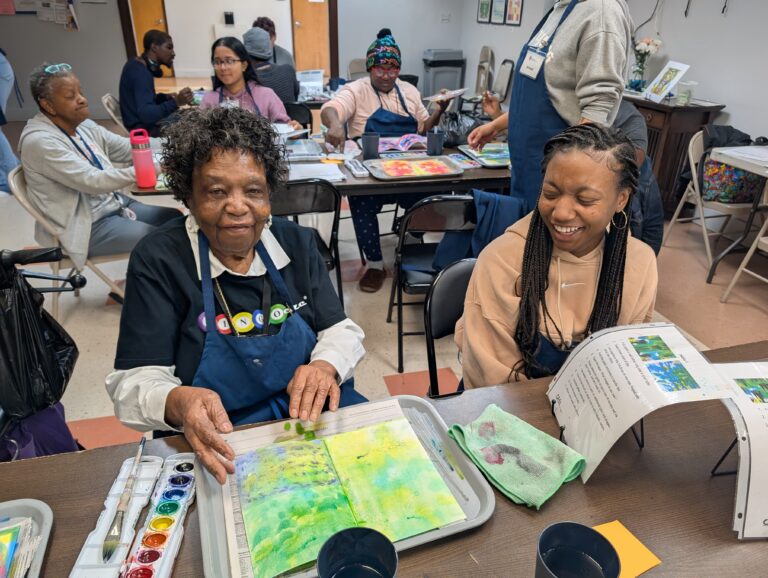 Older lady participant showing green artwork with volunteer.
