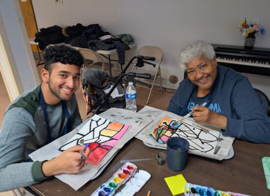 Volunteer and participant smiling while painting geometric art.