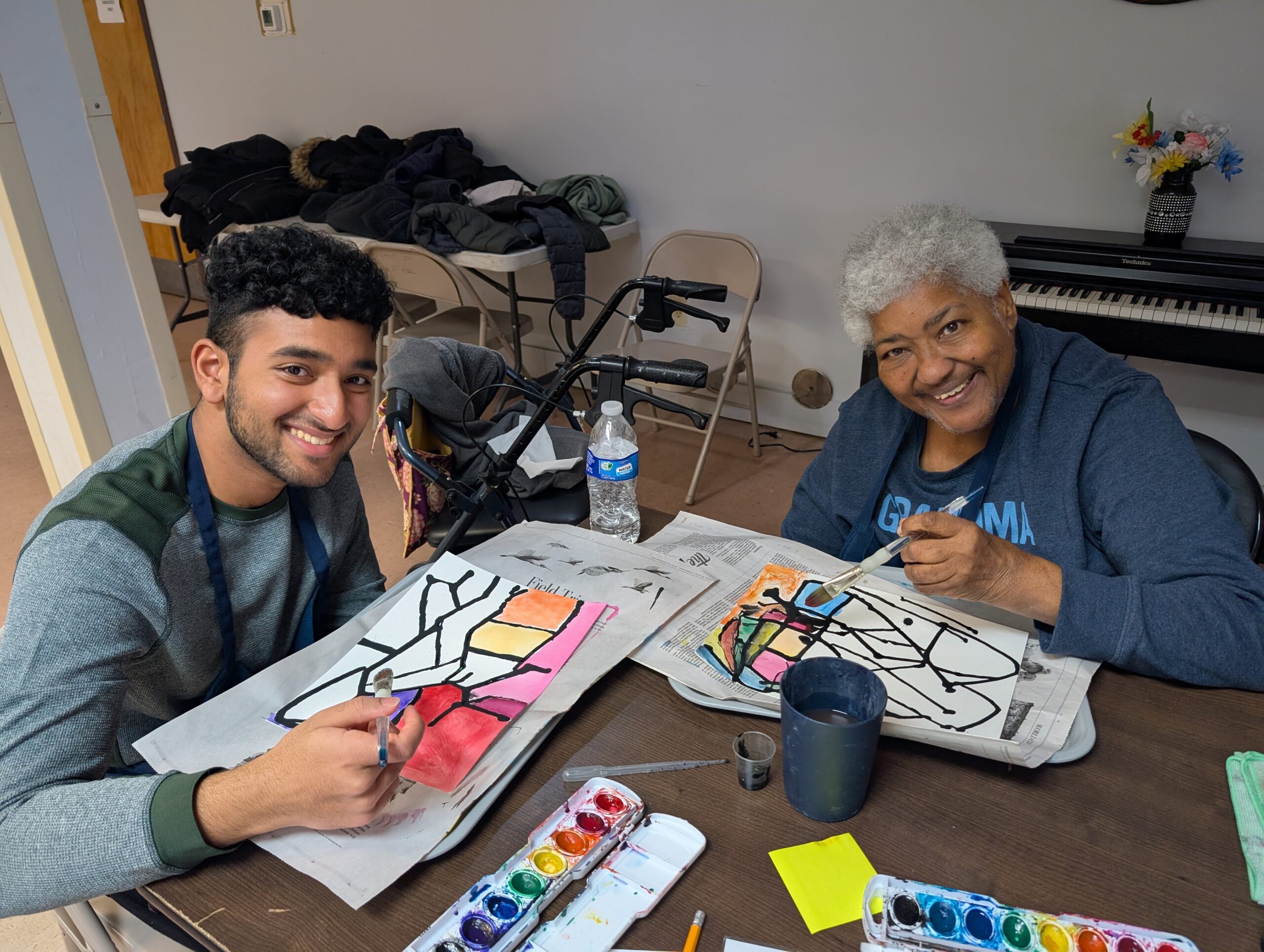 Volunteer and participant smiling while painting geometric art.